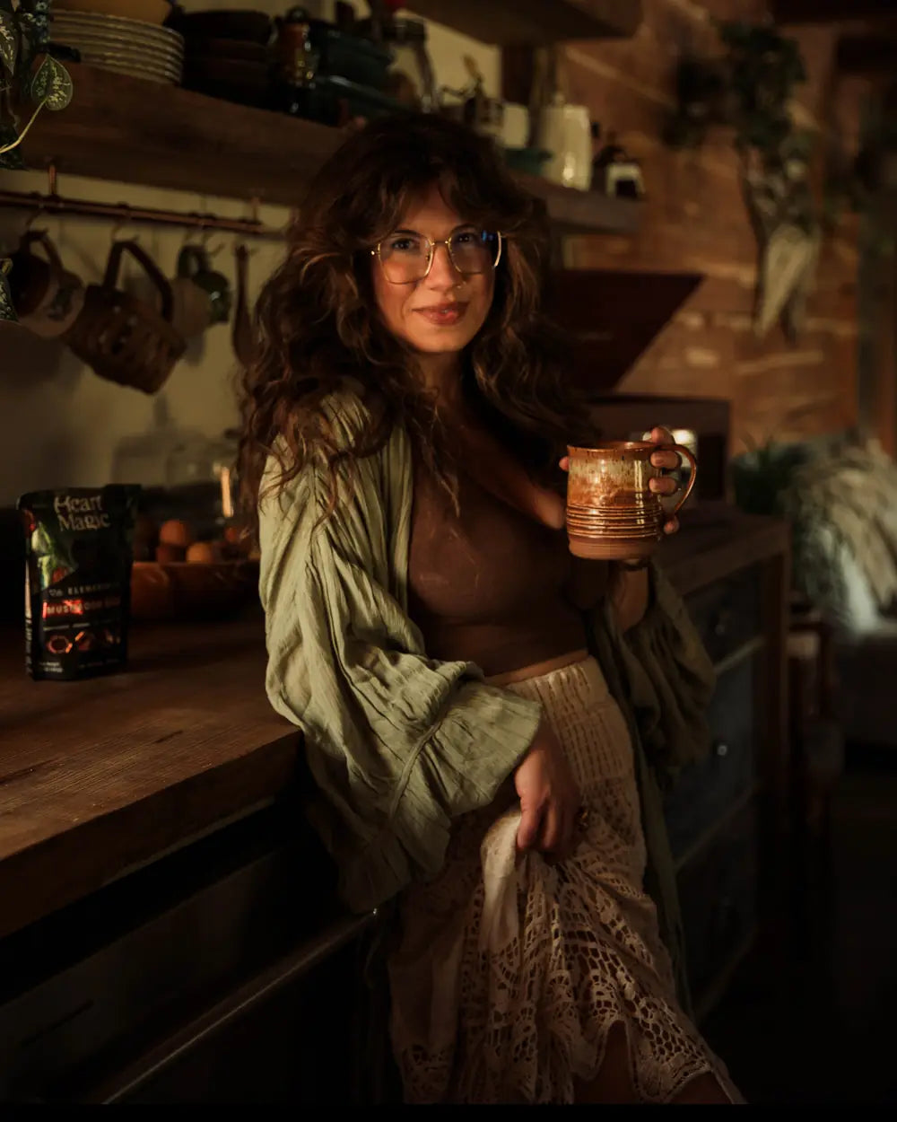 Jeannie smiles in her kitchen holding a mug of Heart Magic cacao, a bag of Elemental on the counter beside her