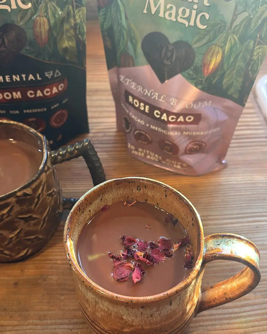 Jeannie's mug of Heart Magic cacao topped with dried rose petals, beside bags of Elemental and Eternal Bloom Rose on her wooden table