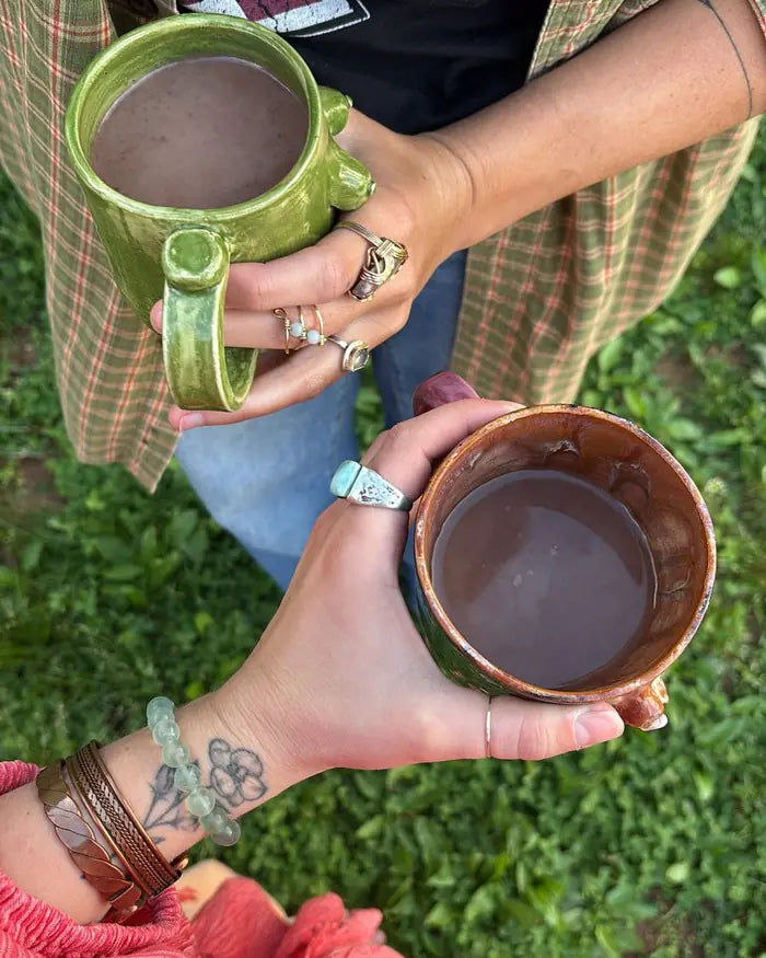 Two people outdoors on the grass, each holding a handmade mug of cacao