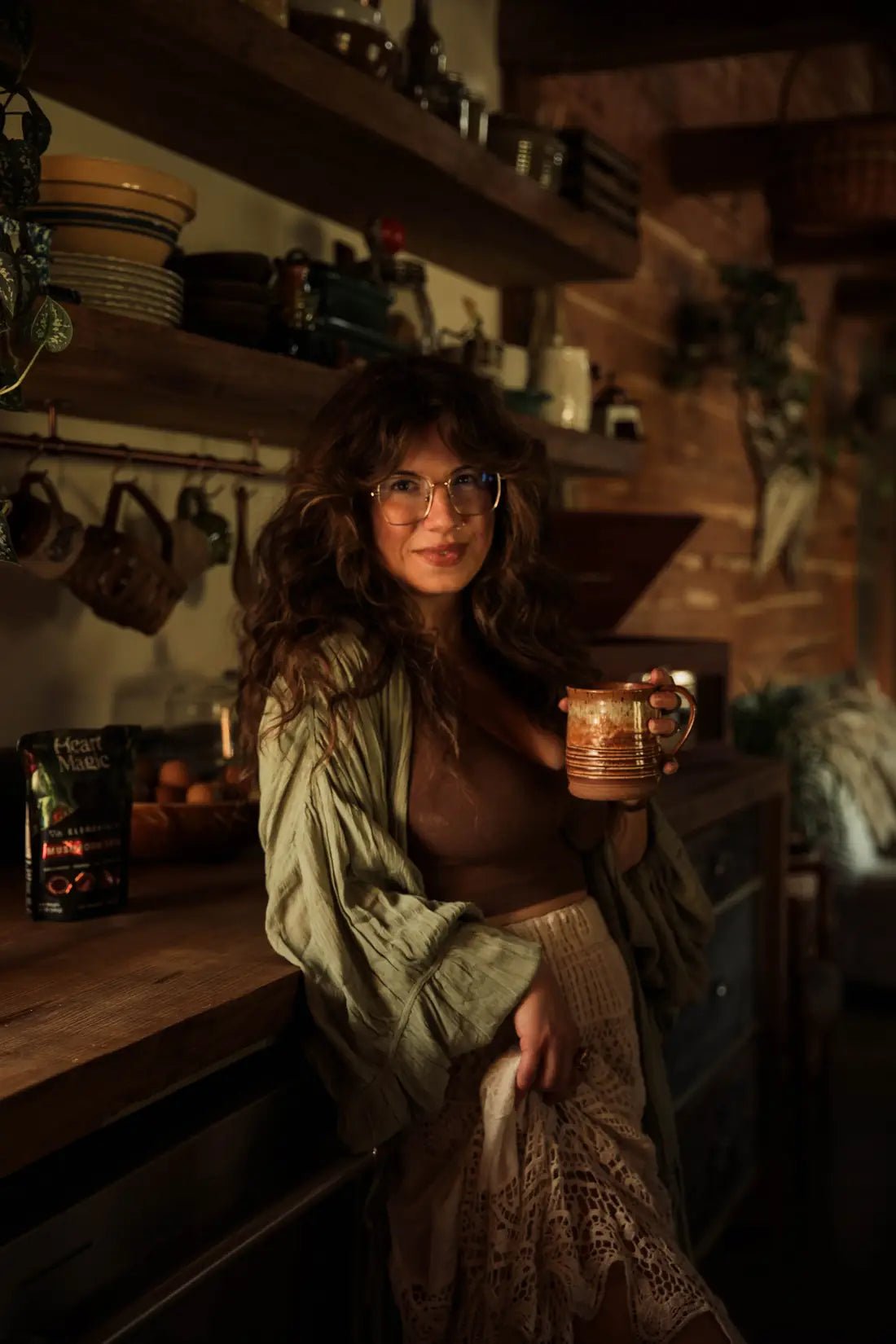 A woman smiling at her kitchen counter with a mug of cacao, a bag of Heart Magic beside her