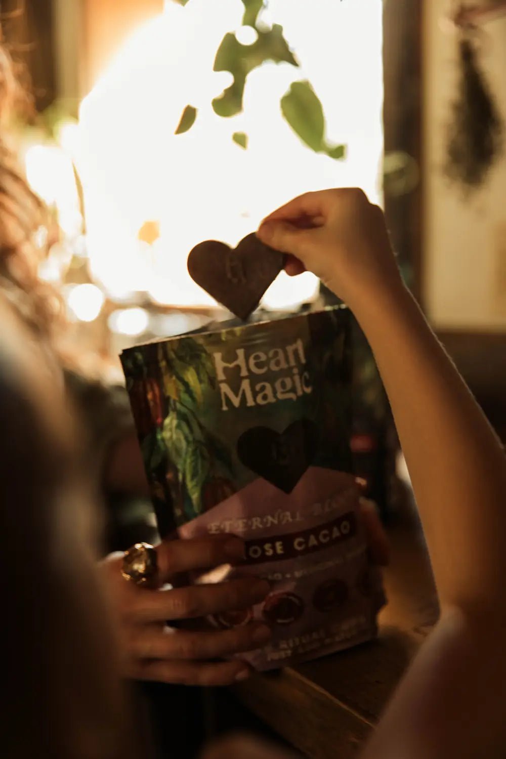 A hand holding up a cacao heart above a bag of Eternal Bloom Rose